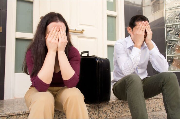 Donna e uomo con mani sul viso e valigia fuori dalla porta di casa