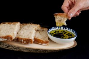persona che intinge un pezzo di pane dentro all'olio e fette di pane su un tagliere