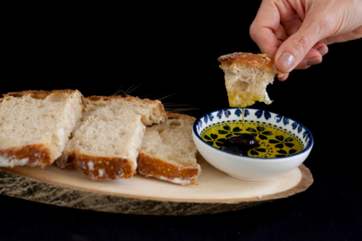 persona che intinge un pezzo di pane dentro all'olio e fette di pane su un tagliere