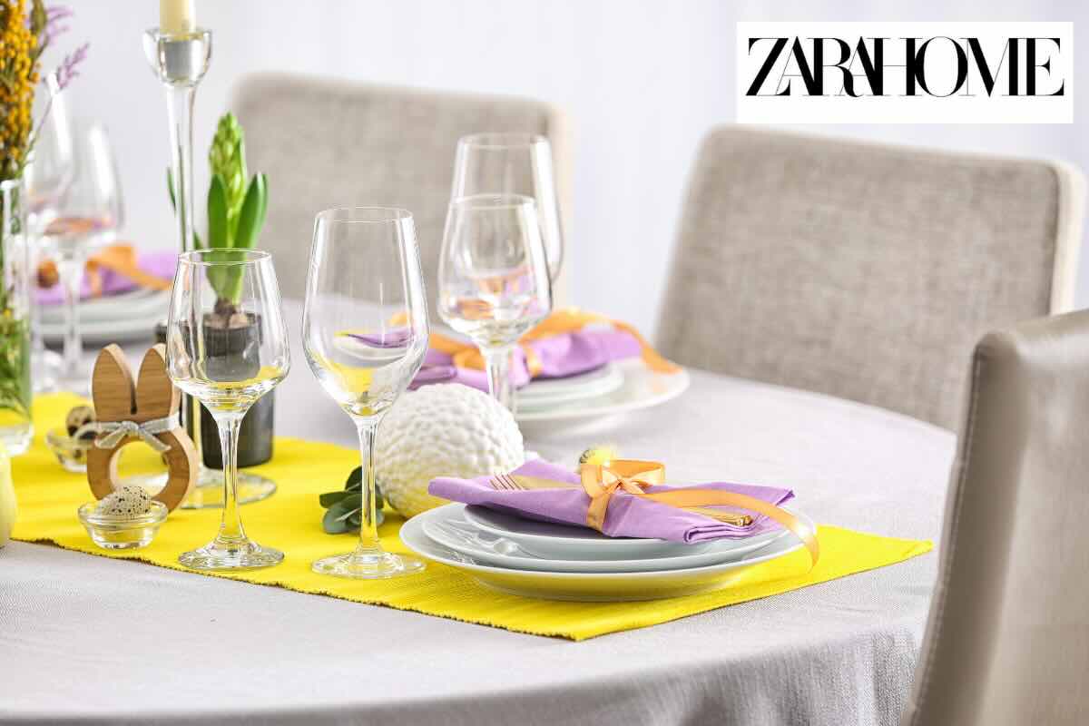 tavola apparecchiata con piatti e bicchieri e runner giallo e scritta zara home
