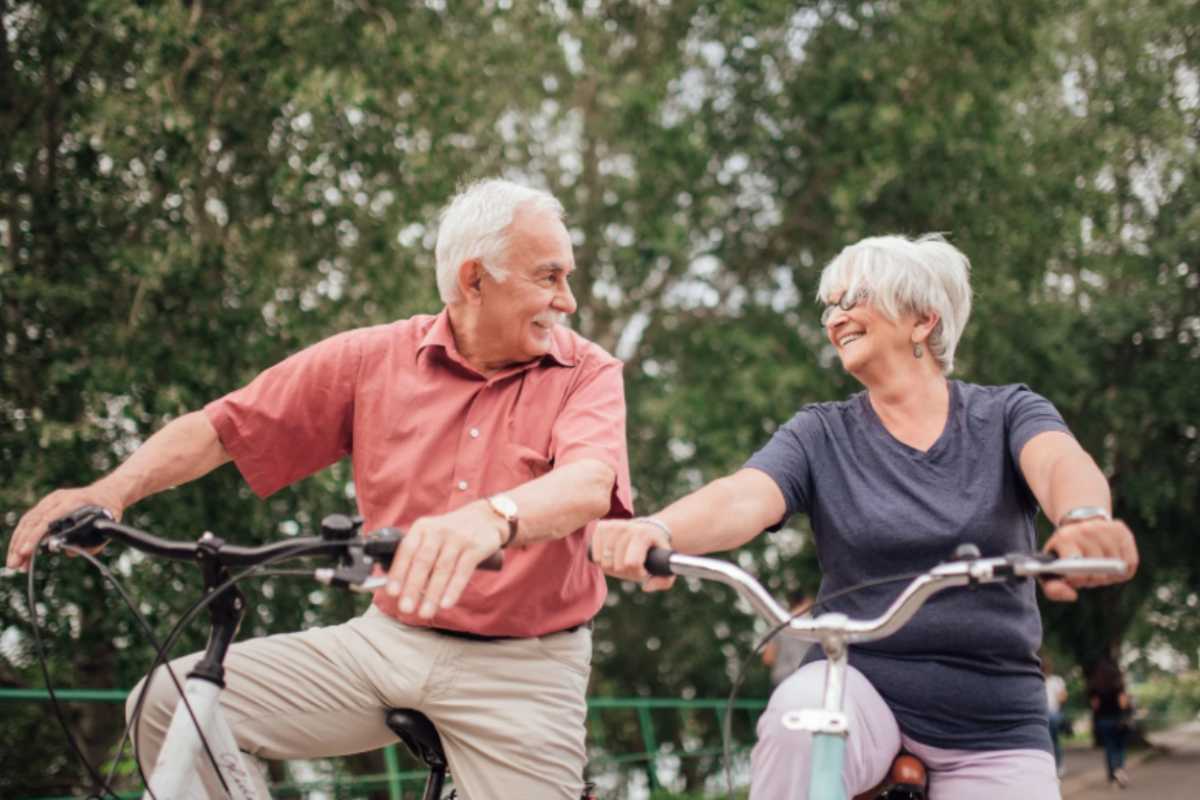 uomo e donna anziani in bicicletta che sorridono